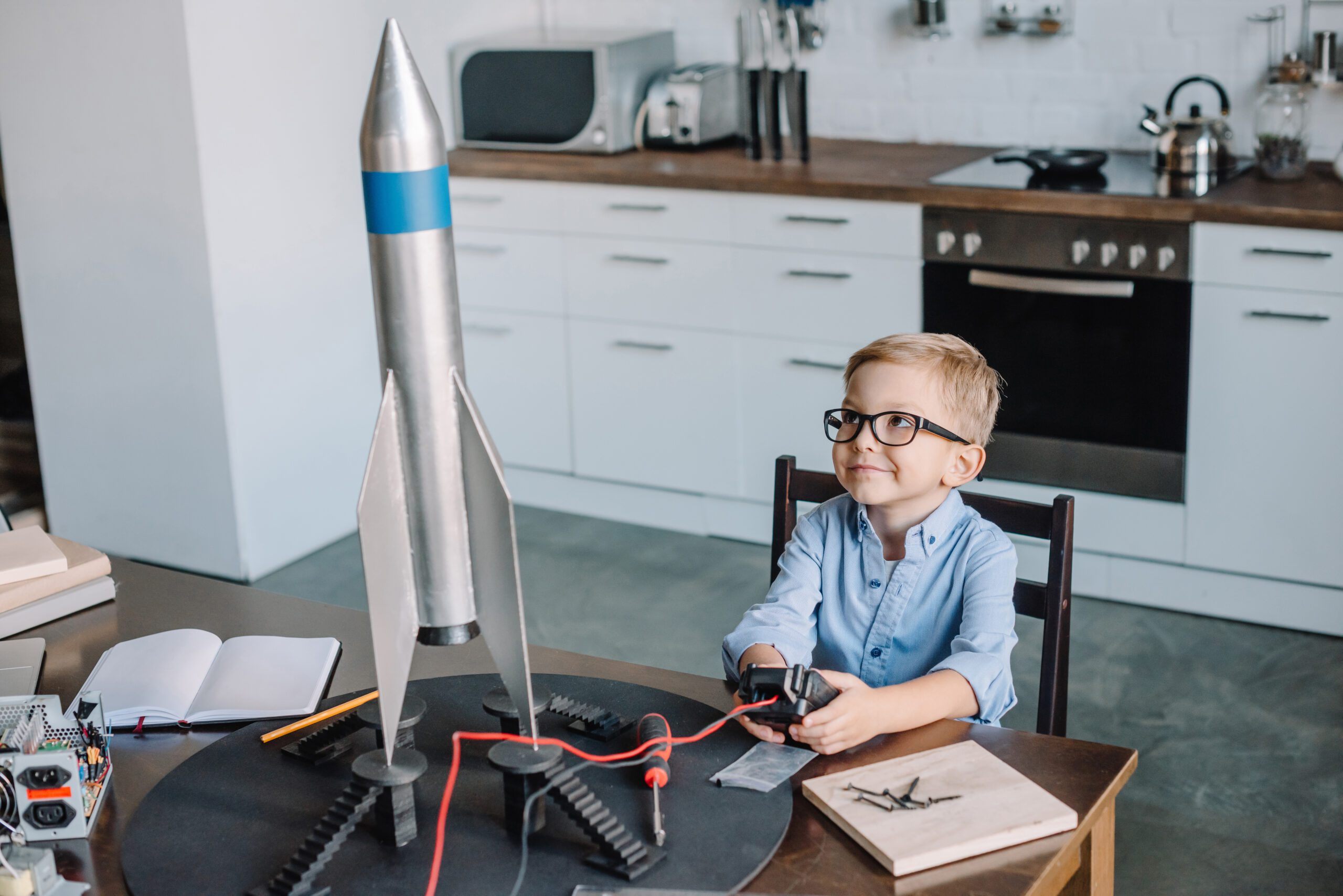 adorable boy sitting at table and testing rocket model in kitchen on weekend